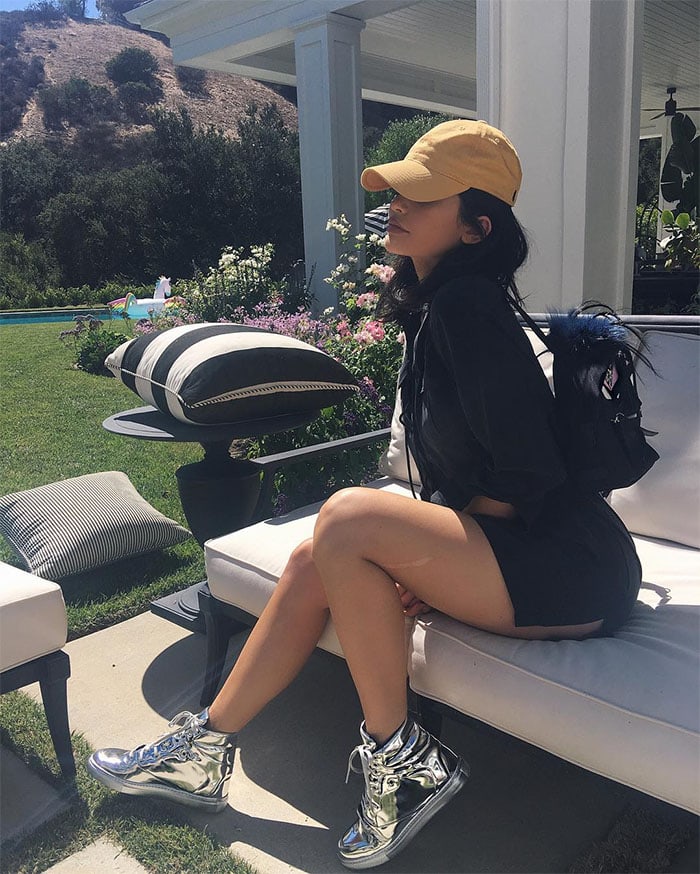 Kylie Jenner rocks a casual yet edgy look in a black hoodie, matching mini shorts, metallic silver high-top sneakers, a mustard cap, and a chic black mini backpack in her Instagram post from July 22, 2016
