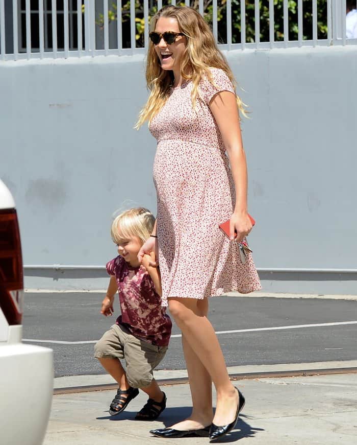 Clad in a tastefully understated printed dress featuring an empire waist and a gracefully flowing skirt, Teresa Palmer exhibited a fashion choice that embraced her evolving silhouette with comfort and ease