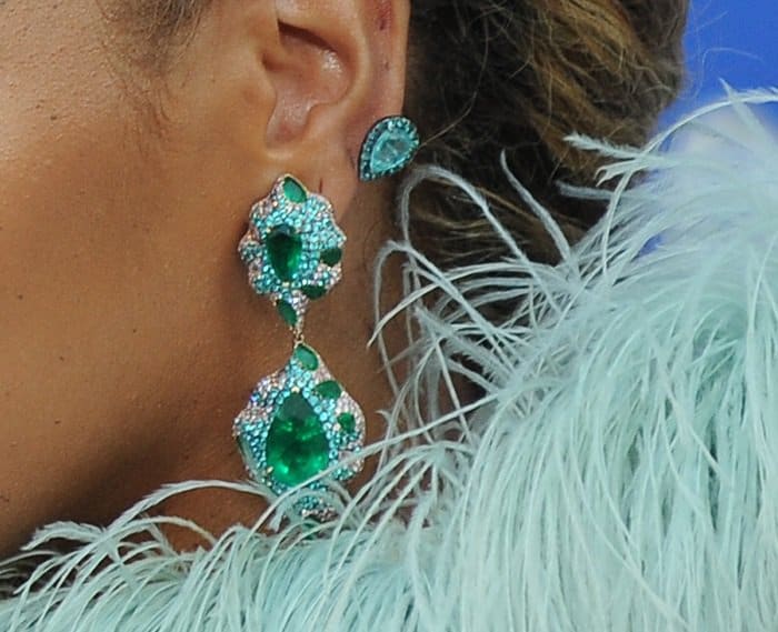 Beyoncé's earrings feature a striking design with large, teardrop-shaped emeralds set in a sparkling halo of diamonds