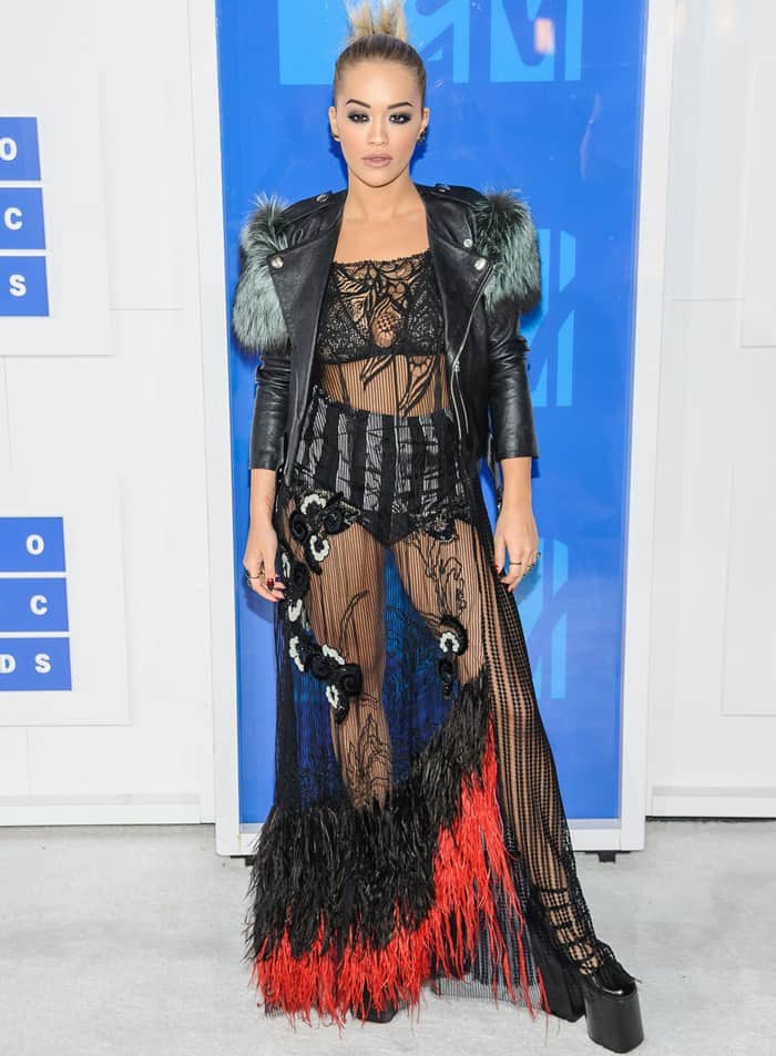 Rita Ora makes a bold statement at the 2016 MTV Video Music Awards in a daring sheer Marc Jacobs gown with feathered accents, paired with a leather jacket and sky-high platform heels