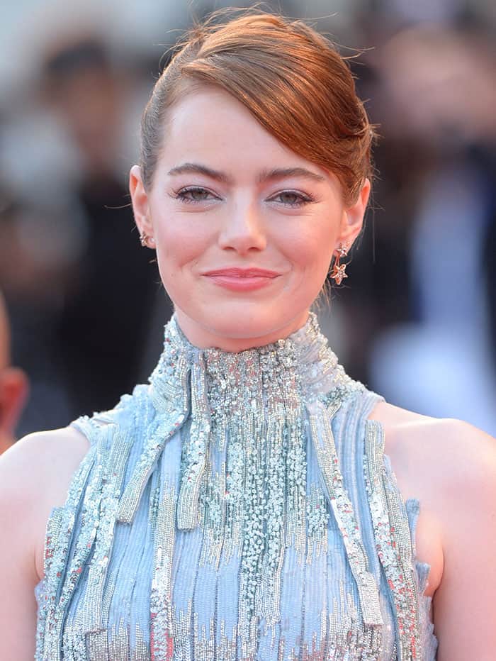 Emma Stone complements her dazzling look with a sleek side-parted updo and soft, glowing makeup, featuring subtle pink lips and delicate eye makeup