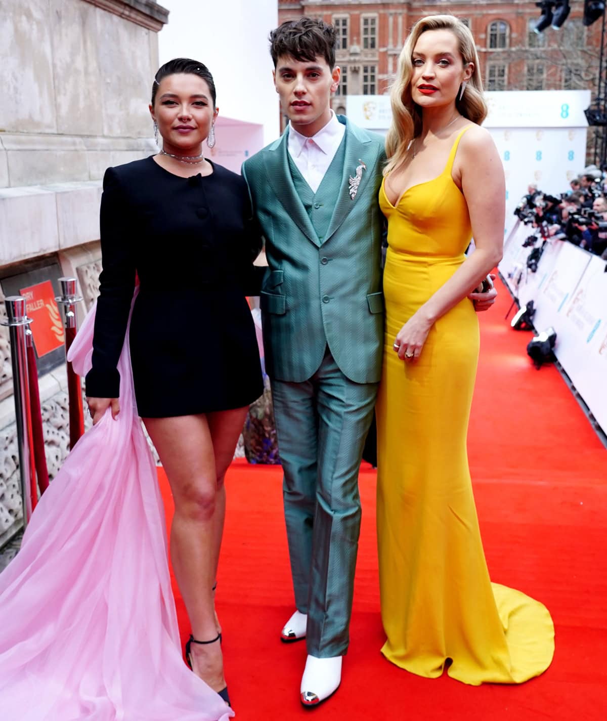 Laura Whitmore stands out with her heels on the red carpet, closely matching Max Harwood's height, while towering over Florence Pugh at the British Academy Film Awards 2022