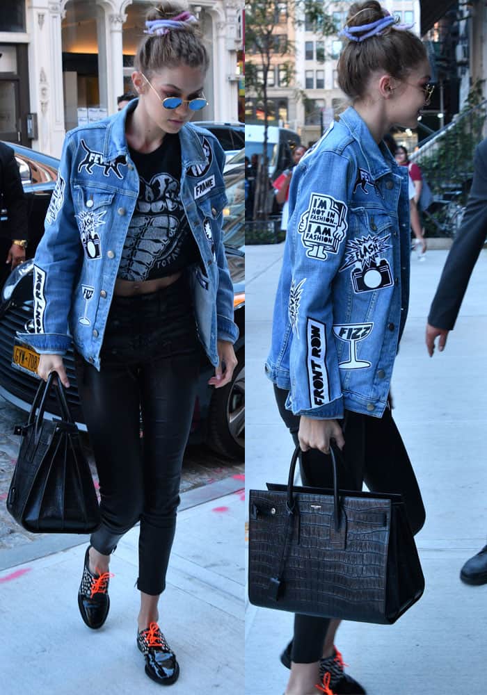 Carrying a classic Saint Laurent "Sac de Jour" tote, Gigi Hadid goes for a vintage look in a customized Frame "Le Original" patch denim jacket paired with Unravel leather pants and a retro graphic crop top