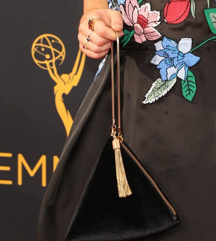 Maisie Williams adds a touch of glamour to the 2016 Emmy Awards with a Charles & Keith triangle-shaped velvet purse, featuring a gold zipper and tassel detail—an affordable yet elegant red carpet statement