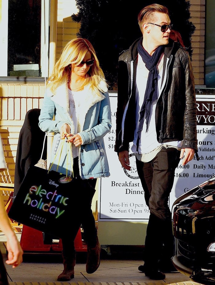 Ashley Tisdale embraces cozy winter style in a light blue shearling-lined jacket, black leggings, and brown suede boots, while Christopher French opts for a rocker-chic look with a black leather jacket, white tee, and black boots as they do some last-minute Christmas shopping at Barneys New York on December 20, 2012