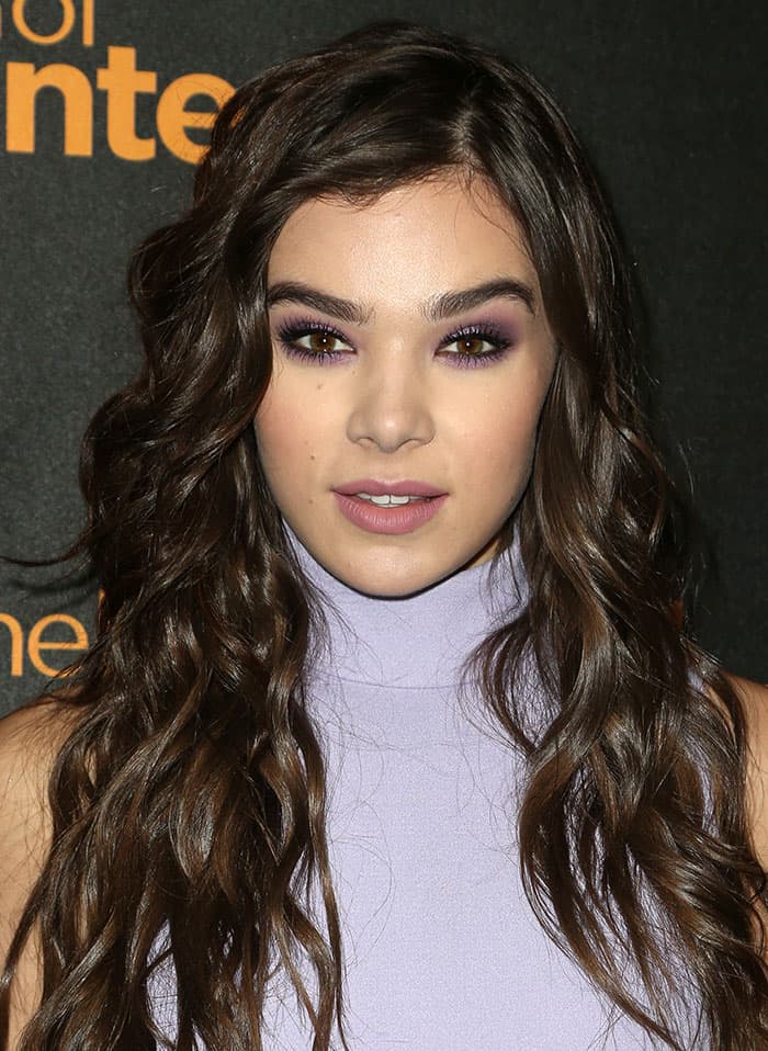 Hailee Steinfeld's long, glossy tresses cascaded in flowing waves over her shoulders, complemented by bold purple eye makeup, mascara, and a matte lip shade to complete the dramatic look