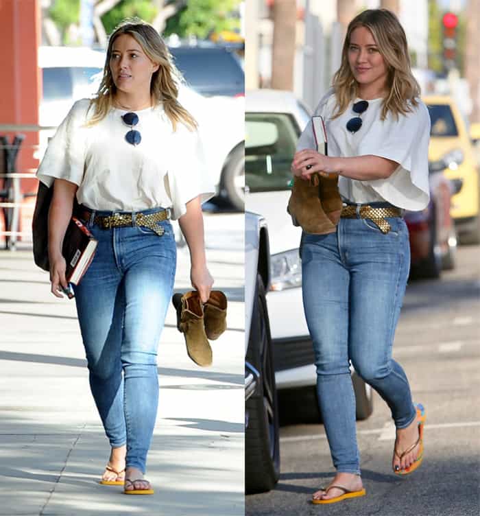 Hilary Duff is carrying a pair of brown ankle boots in one hand and a book in the other