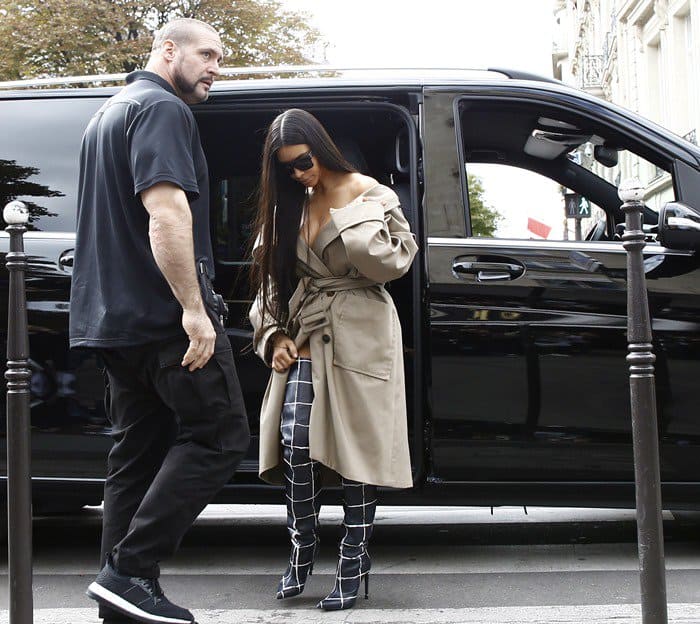 Kim Kardashian steps out in style wearing a chic trench coat and plaid boots at Paris Fashion Week, accompanied by her bodyguard, Pascal Duvier
