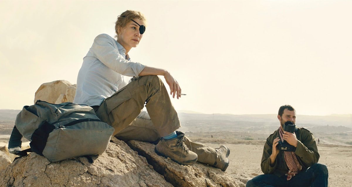 Rosamund Pike, portraying war correspondent Marie Colvin, wears rugged combat boots and utilitarian cargo pants alongside Jamie Dornan as photographer Paul Conroy in A Private War