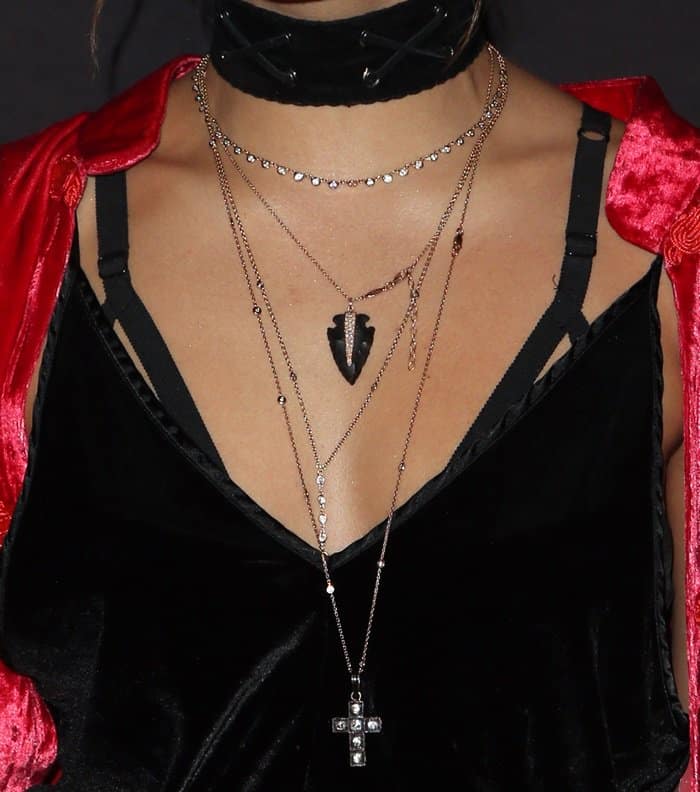 Vanessa Hudgens layers her necklaces for a gothic-inspired look, featuring a statement cross pendant, an arrowhead charm, and a studded choker