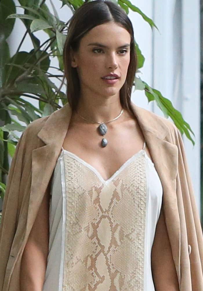 Alessandra Ambrosio lets her natural beauty shine, wearing minimal makeup and sleek, straight hair to complement her chic snakeskin dress and earthy trench coat