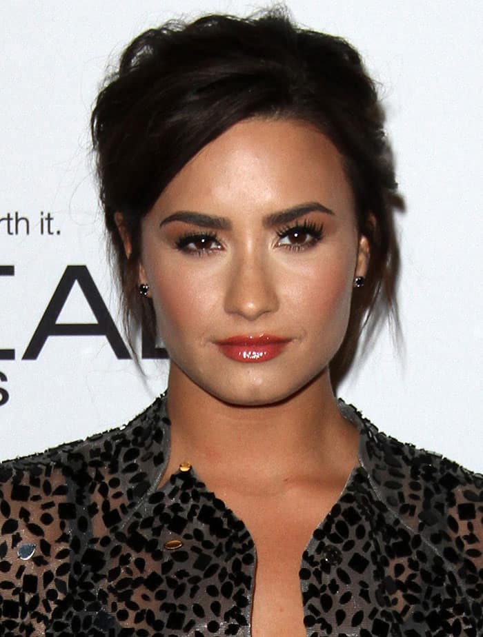 Demi Lovato's glossy lips, in a soft nude shade, enhance her natural beauty, while her subtle black stud earrings complete the look with understated elegance