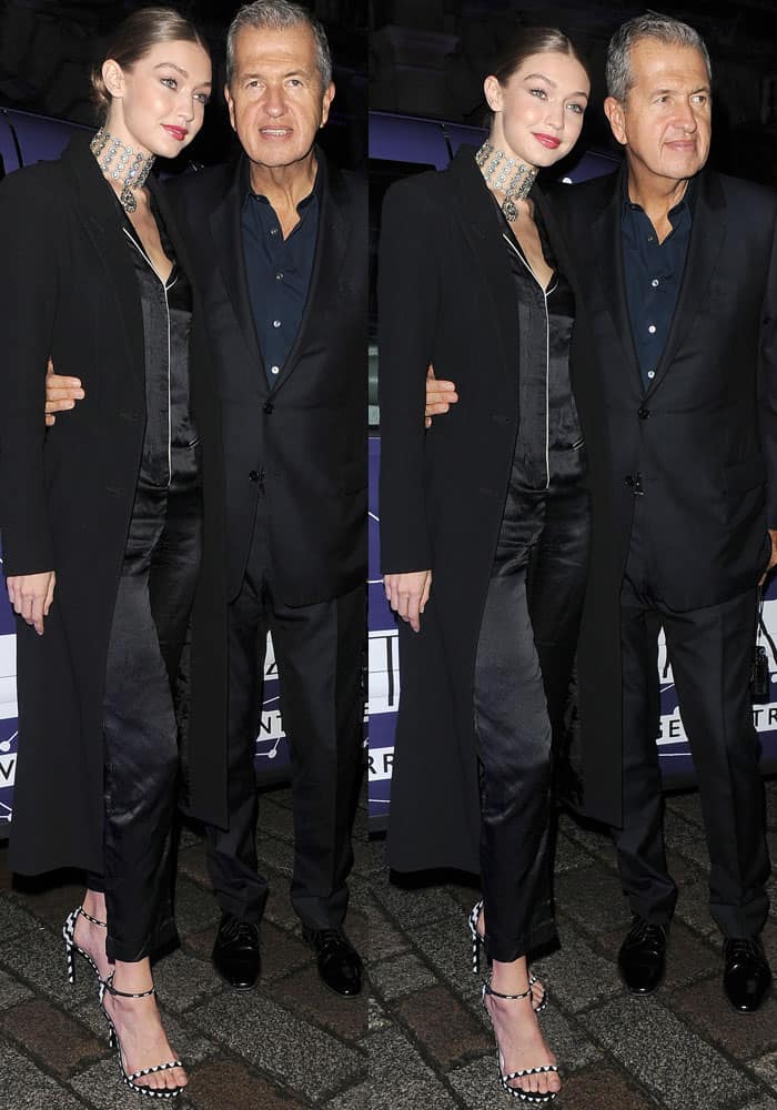 Gigi Hadid stuns in a sleek silk jumpsuit paired with a chic black coat and beaded Stuart Weitzman "Nudist" sandals as she poses alongside Mario Testino at the Stuart Weitzman VIP dinner in London