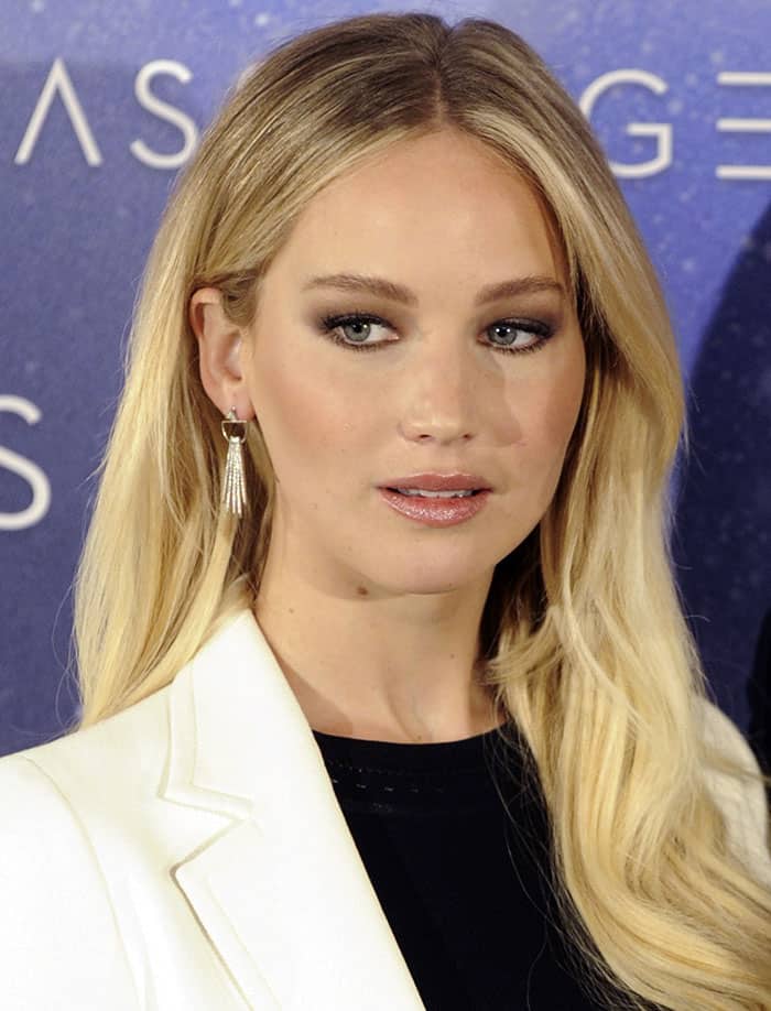 Jennifer Lawrence complements her look with delicate tassel earrings, hair styled in soft blonde waves, while her subtle smoky eyes highlight her striking blue eye color