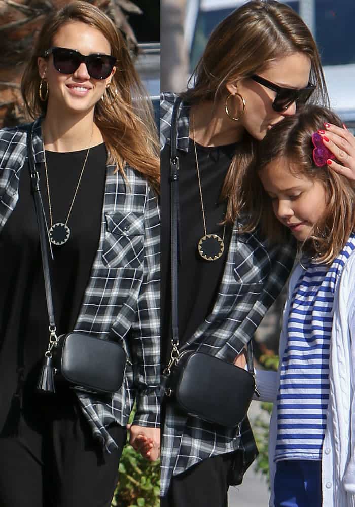 Jessica Alba steps out in a casual black midi dress layered with a plaid shirt and accessorized with a Pop & Suki camera bag and hoop earrings while spending time with her daughter in West Hollywood