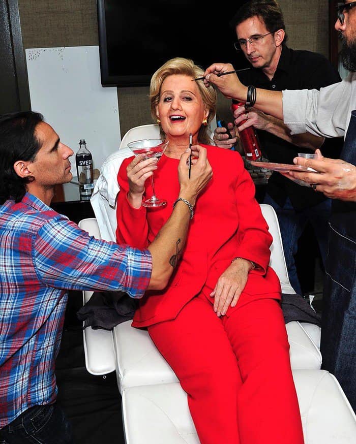 Katy Perry enjoys a drink in the makeup chair while she gets help to transform into Hilary Clinton