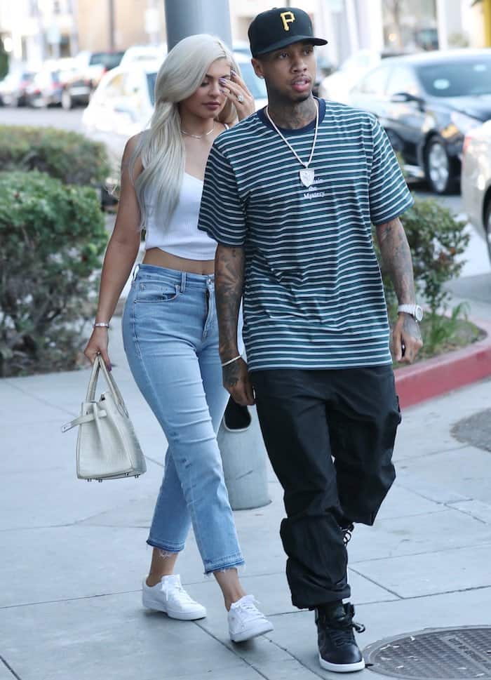 Tyga keeps it laid-back in a striped Supreme t-shirt, baggy black pants, black high-top sneakers, and a Pittsburgh Pirates cap, accessorized with a chain necklace, as he steps out with Kylie Jenner for a lunch date