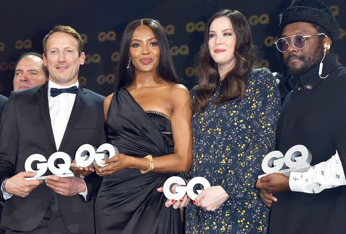 Liv Tyler stands alongside fellow honorees Naomi Campbell and will.i.am at the GQ Men of the Year Awards, radiating elegance in her floral dress while accepting the Gentlewoman of the Year award