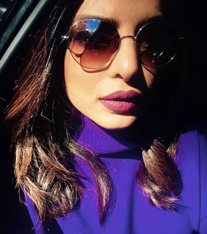 Priyanka Chopra rocks reflective Garrett Leight sunglasses and a purple long-sleeve mini dress featuring a high collar