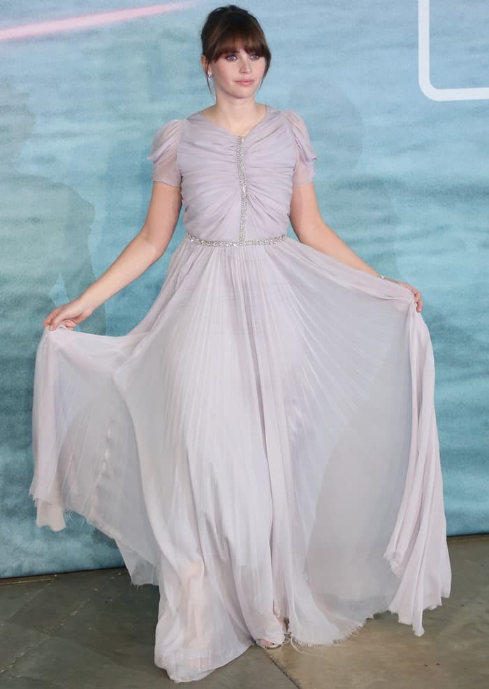 Felicity Jones elegantly holds out the flowing skirt of her Giambattista Valli gown, showcasing its delicate pleats and ethereal design at the 'Rogue One: A Star Wars Story' London premiere