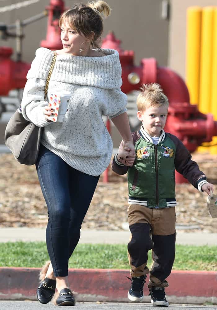 Hilary Duff steps out with her son Luca, rocking a cozy off-shoulder sweater, skinny jeans, and fur-lined Gucci Princetown mules while holding a coffee and Luca's hand during their day out