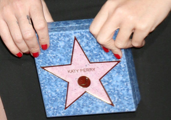 Katy Perry flaunts her red manicure and small finger tattoos while holding her personalized Charlotte Olympia 'Walk of Fame' clutch
