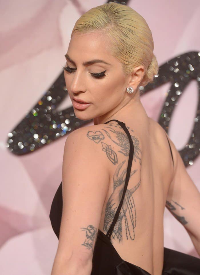 Lady Gaga proudly displays her intricate tattoos, including a large hand motif and floral designs