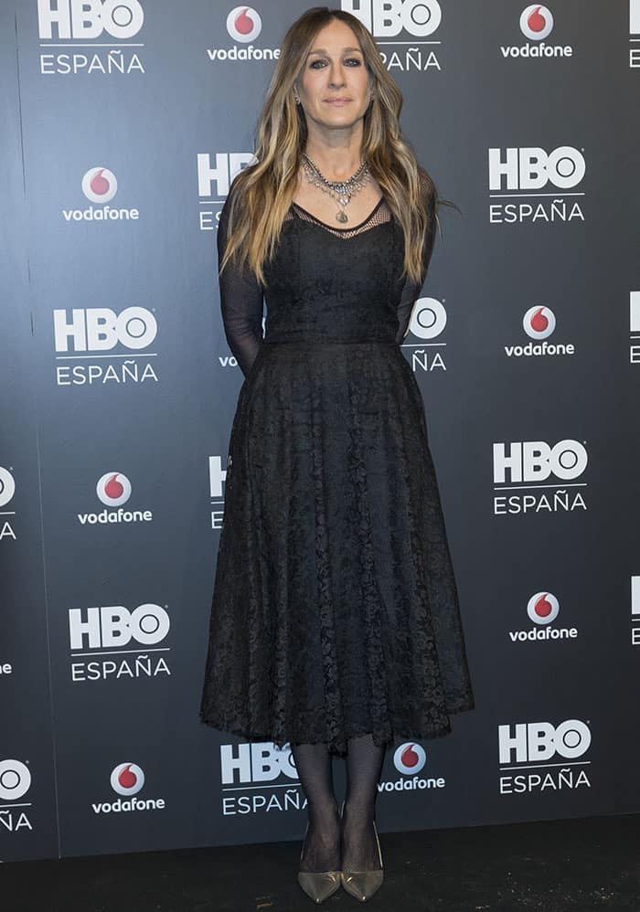 Sarah Jessica Parker embodies timeless sophistication in a classic black lace midi dress accentuated by layered necklaces and chic metallic pumps