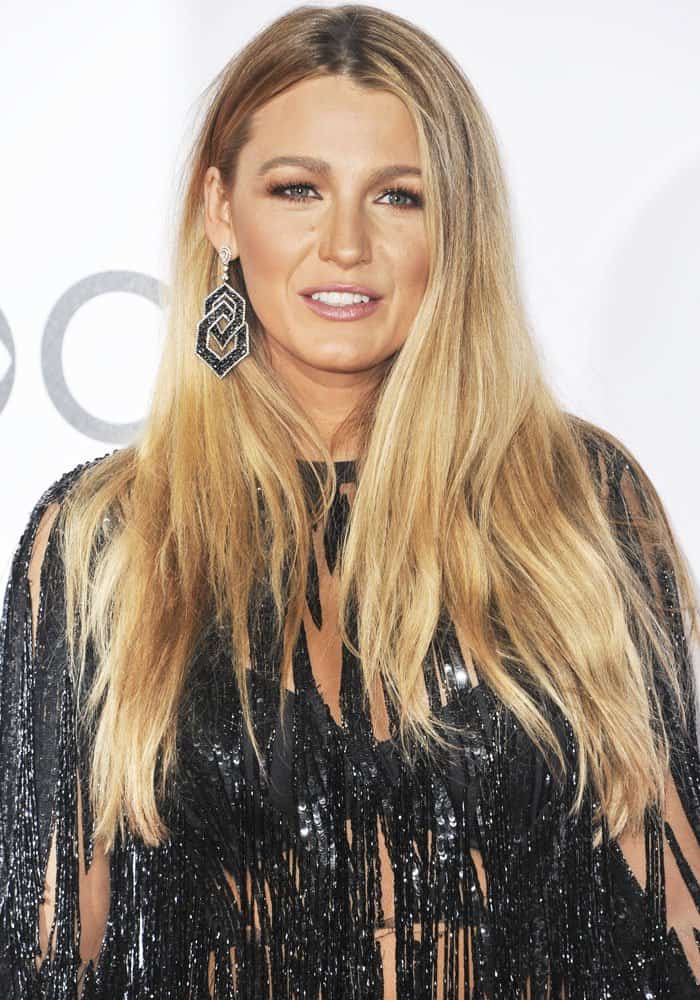 Blake Lively completes her look with geometric statement earrings, soft waves, and a glowing makeup palette featuring neutral tones and a subtle pink lip