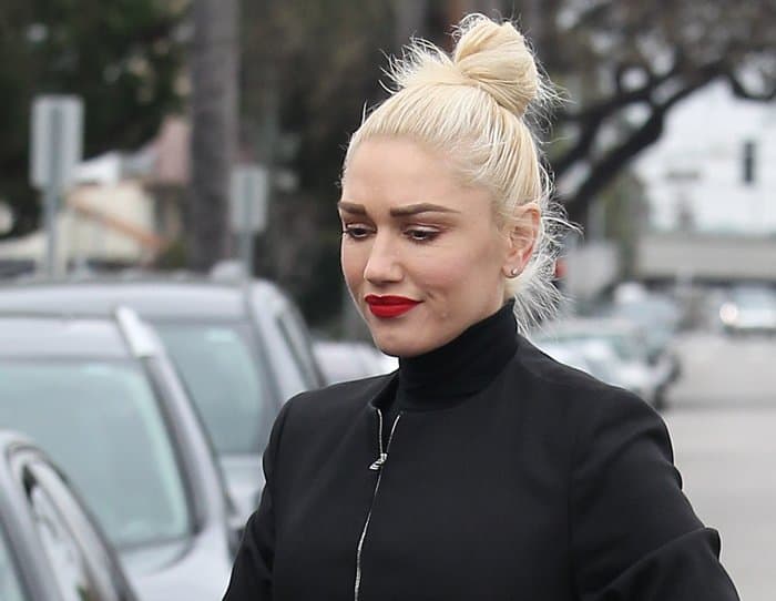 Gwen Stefani keeps it sleek with a platinum blonde topknot bun, classic diamond stud earrings, and a bold red lip for a polished off-duty look