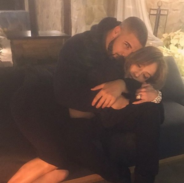 Drake and Jennifer Lopez share an intimate moment, cuddling on a sofa in a cozy setting