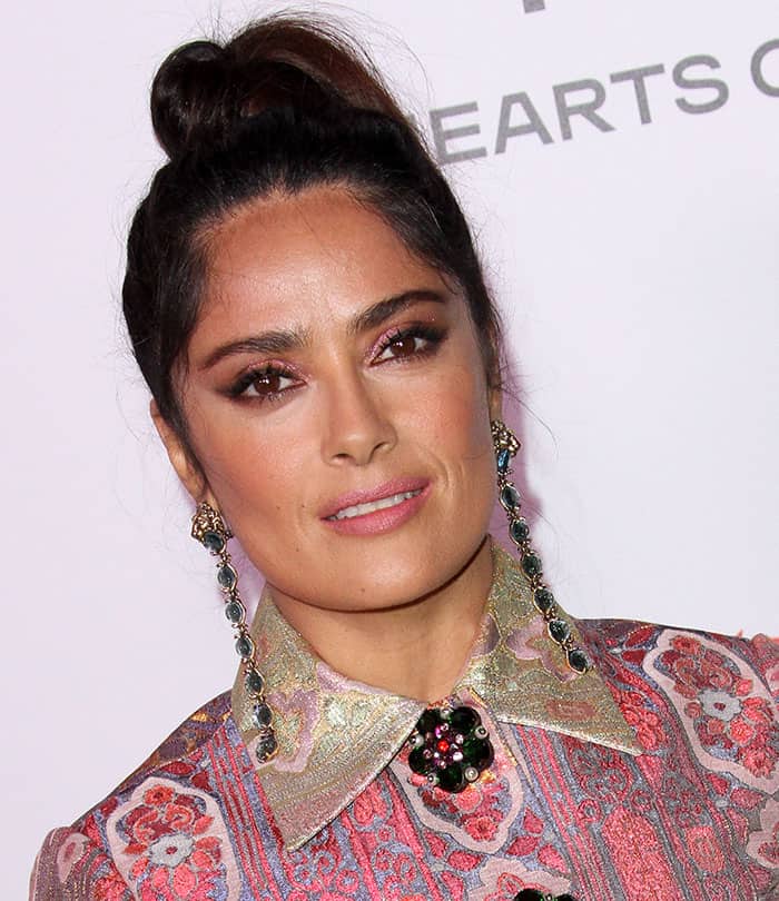 Salma Hayek stuns with emerald green chandelier earrings that perfectly complement her radiant brown eyes and shimmering pink eyeshadow