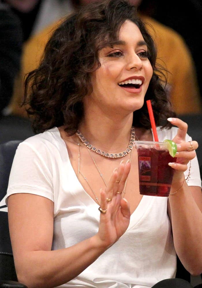 Vanessa Hudgens keeps it effortlessly chic courtside in a simple white v-neck tee, layered necklaces, and radiant curls