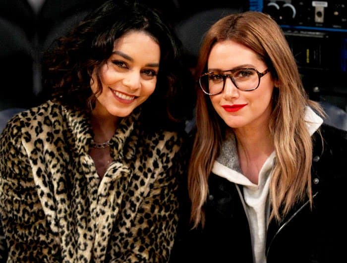 Vanessa Hudgens rocks a chic faux leopard coat, while Ashley Tisdale stuns in a sleek leather jacket and bold glasses courtside
