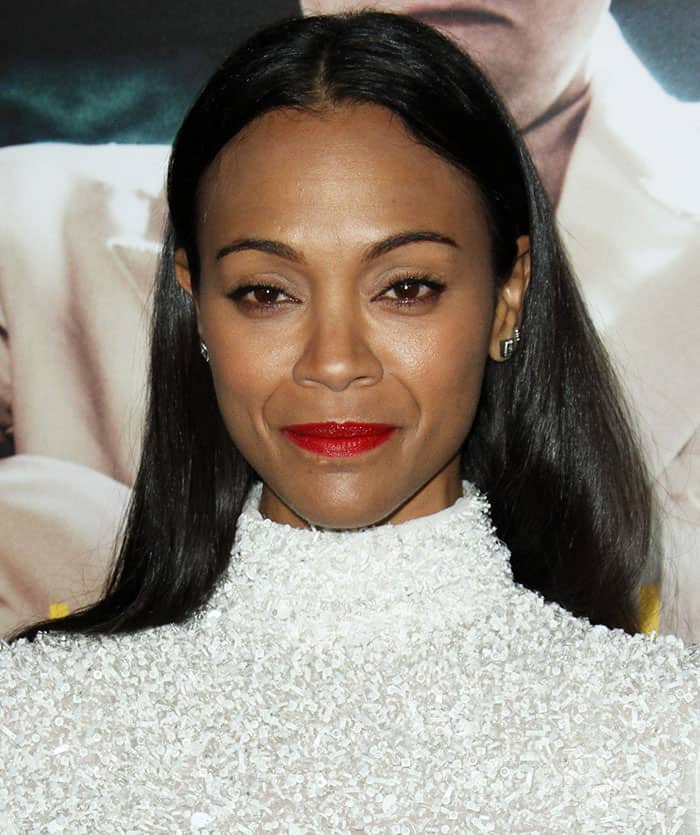 Zoe Saldaña completes her sophisticated look with a bold red lip, sleek straight hair, and understated diamond earrings, proving that minimal jewelry can make a powerful statement