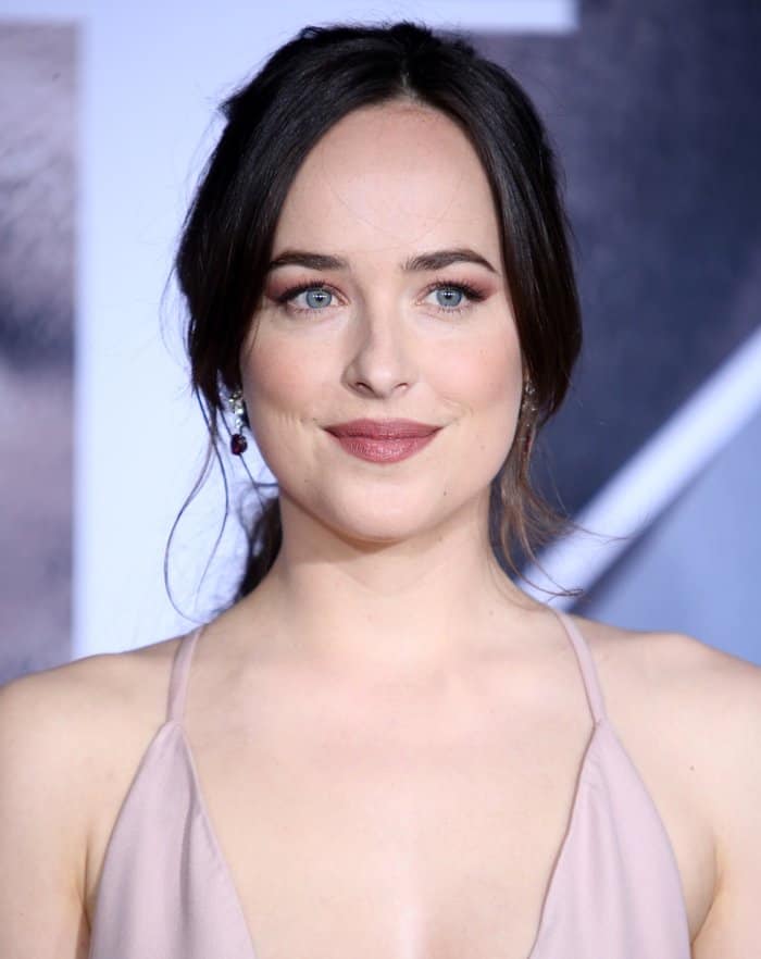 Dakota Johnson stuns with her soft updo, romantic mauve-toned makeup, and delicate drop earrings that add a touch of understated glamour to her red-carpet look
