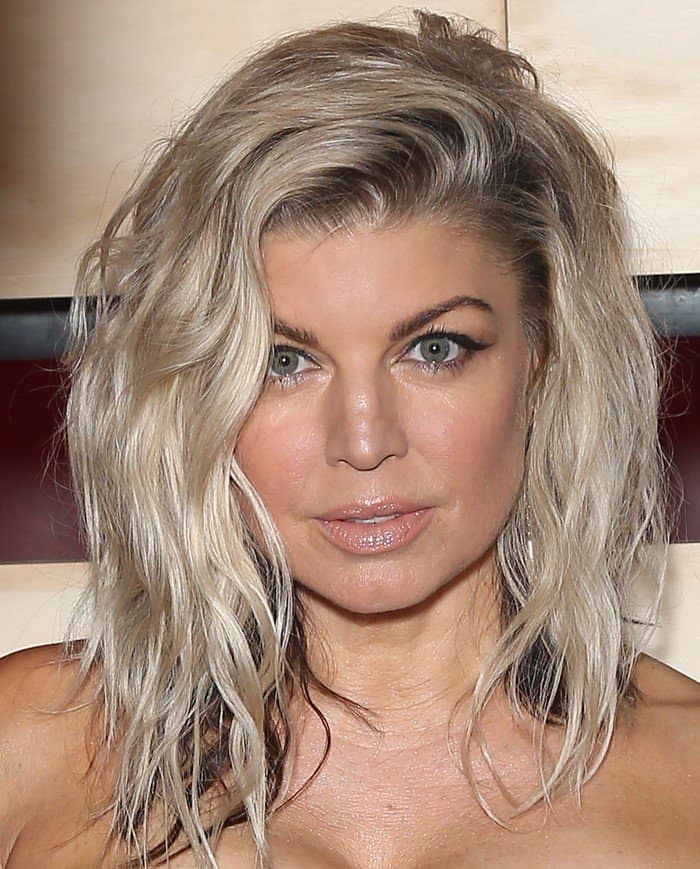 Fergie's striking blue-green eyes are accentuated with soft black eyeliner, defined brows, and subtle shimmering eyeshadow