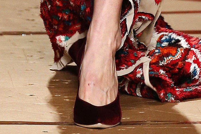 Gigi Hadid navigates the runway in Moschino's luxurious red velvet pumps, which momentarily snagged on the fringed hem of her bold, statement-making gown at the Fall 2017 fashion show