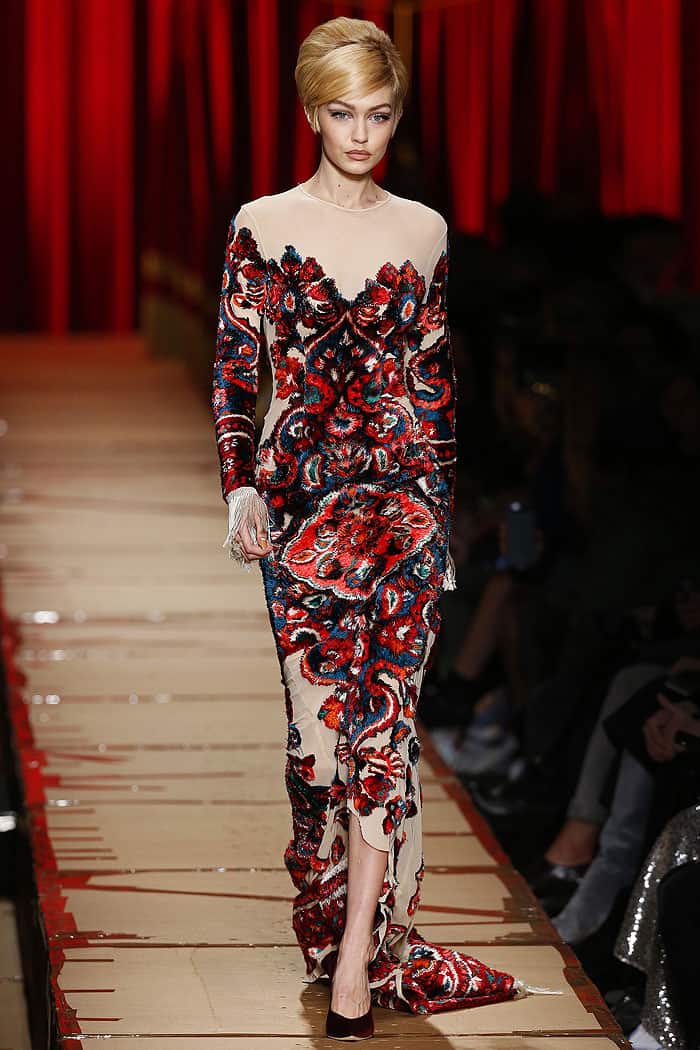 Gigi Hadid commands the runway at the Moschino Fall 2017 fashion show during Milan Fashion Week Fall/Winter 2017/18, effortlessly showcasing a bold, tapestry-inspired gown with intricate embroidery and dramatic fringe detailing on February 23, 2017, in Milan, Italy