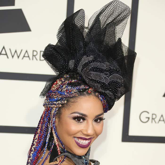 Joy Villa adds a dramatic flair to her look with colorful braided hair and a bold black sculptural headpiece at the Grammy Awards