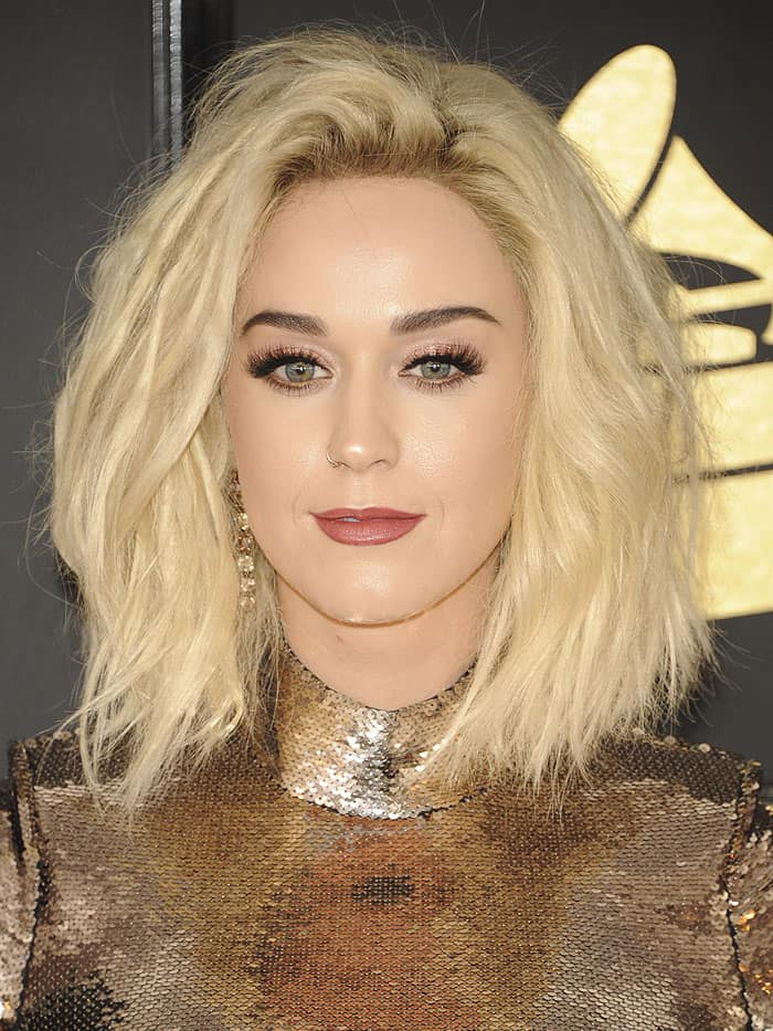 Katy Perry complements her Grammy look with a voluminous, tousled blonde bob and bold makeup, featuring smoky eyes and a soft, matte mauve lip