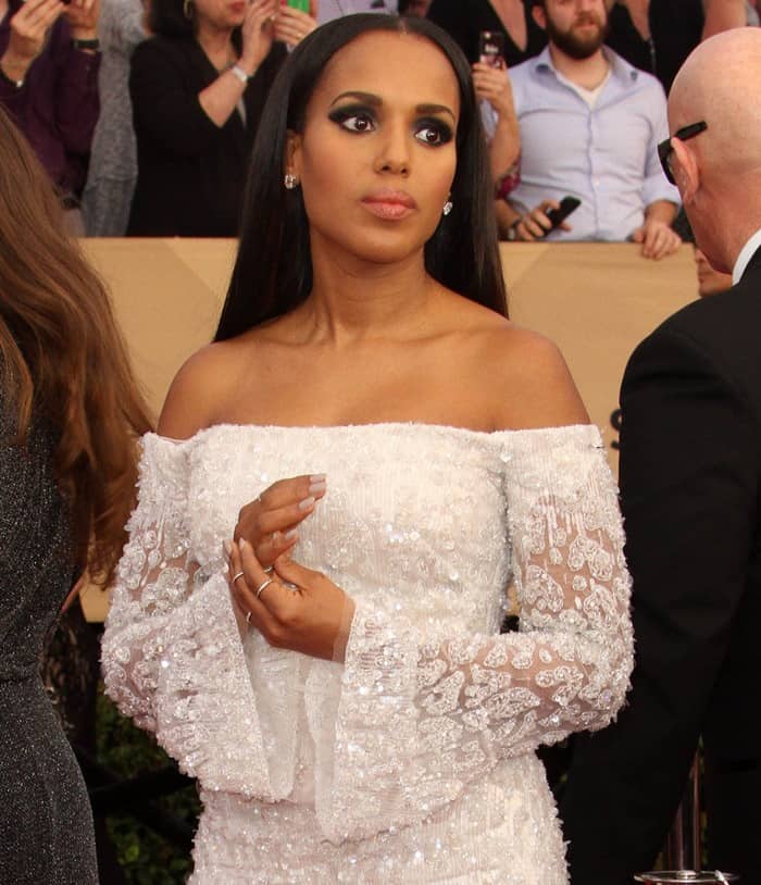 Kerry Washington styled her sleek, straight hair in a center part, perfectly complementing her off-the-shoulder white gown adorned with intricate lace details and shimmering embellishments, featuring flared bell sleeves for an elegant touch