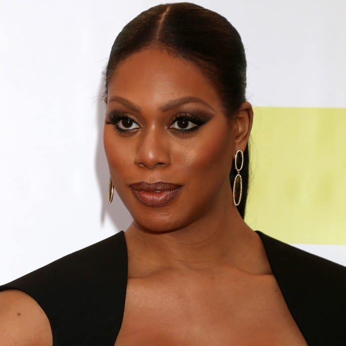 Laverne Cox stuns with a sleek ponytail and dramatic smoky eye makeup, perfectly complementing her elegant black gown and gold statement earrings