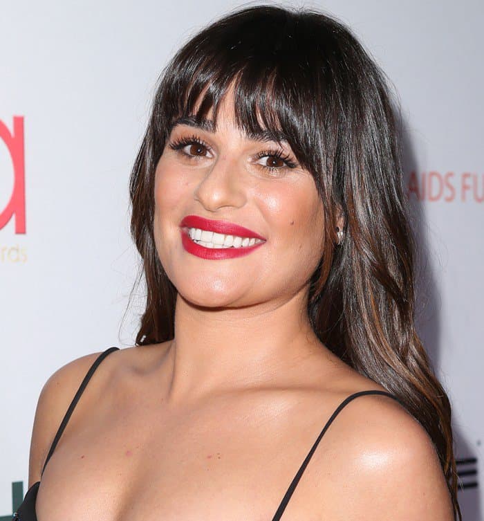 Lea Michele radiates elegance with her bold red lipstick, soft, dewy skin, and perfectly styled bangs framing her glowing smile