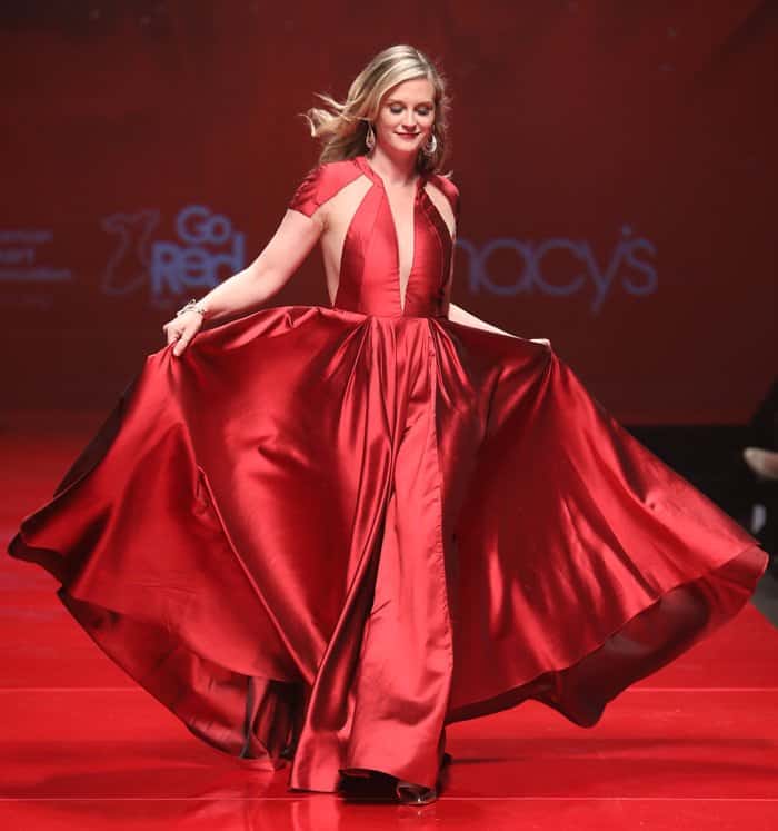 Bonnie Somerville lights up the runway in a dramatic red satin gown featuring a plunging neckline and flowing skirt, capturing the essence of grace and confidence
