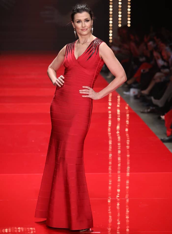 Bridget Moynahan commands the runway in a sleek, figure-hugging red bandage gown accented with sparkling embellishments on the shoulders, radiating poise and elegance
