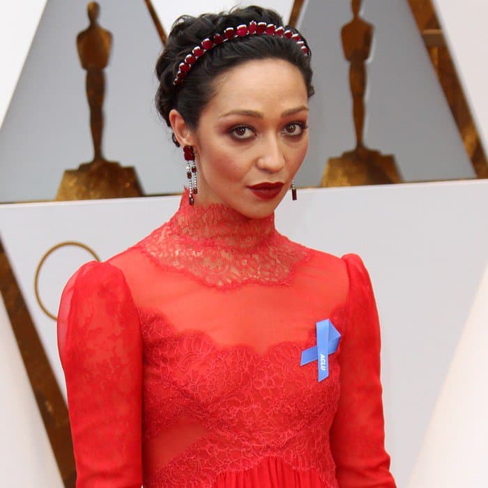 Ruth Negga complements her Valentino gown with a jeweled red headband, bold drop earrings, and an ACLU ribbon