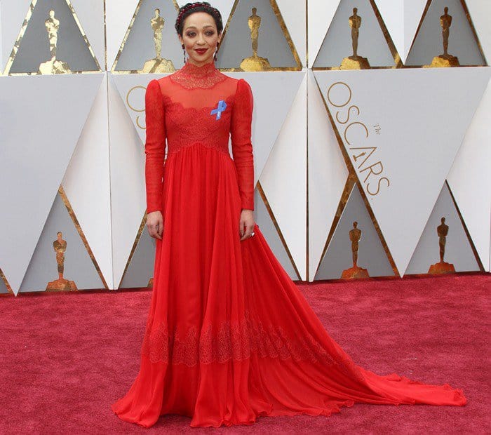 Ruth Negga stuns on the red carpet in a floor-length Valentino gown paired with a jeweled headband, elegant drop earrings, and an ACLU ribbon, showcasing how to balance bold fashion with meaningful advocacy