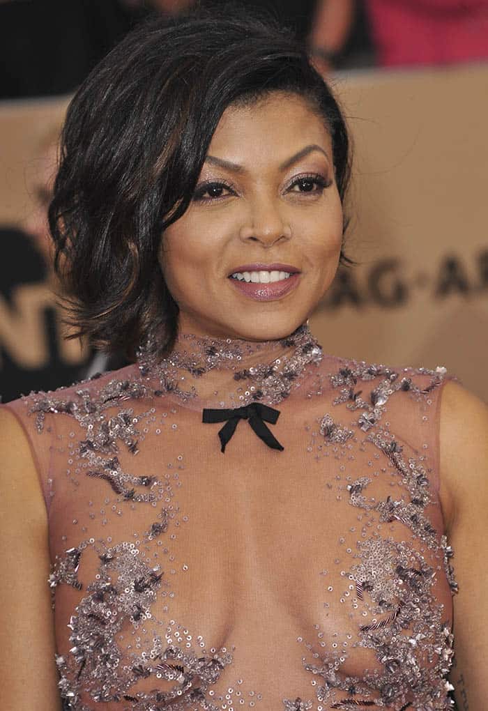 Taraji P. Henson stuns with her textured side-swept bob, shimmering mauve makeup, and delicate detailing on her sheer embellished gown, tied together with a subtle black bow accent