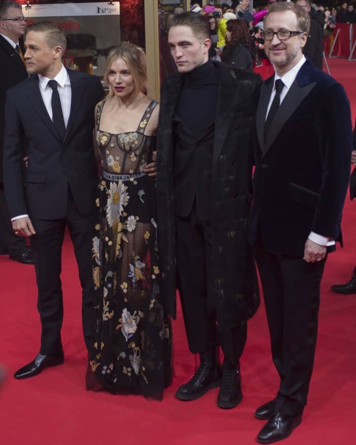 Sienna Miller stuns in a sheer floral-embroidered Christian Dior gown alongside co-stars Charlie Hunnam and Robert Pattinson, who bring sharp suits and edgy elegance to the red carpet